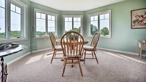 A dining area with a round table and four chairs, large windows with a view, and a carpeted floor. - Blue Birds Perch: Stunning Home on Private Hilltop (Shipshewana)