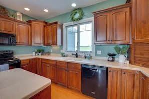 A kitchen with wooden cabinets, a dishwasher, a microwave, and a window with a wreath. - Blue Birds Perch: Stunning Home on Private Hilltop (Shipshewana)