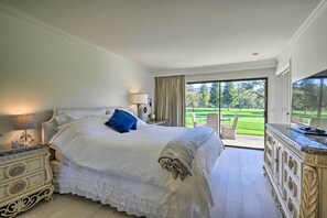 A large bed with a white bedspread and blue pillow, a nightstand with a lamp, and a dresser with a mirror. - Bright & Airy Napa Condo W/patio on Golf Course! (Napa)