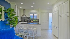 A modern kitchen with white cabinetry, a marble countertop, and a large window. There is a blue sofa and two white chairs in the adjacent living area. - Bright & Airy Napa Condo W/patio on Golf Course! (Napa)