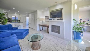 A modern living room with a blue sectional sofa, a glass coffee table, a fireplace, and a TV mounted above it. - Bright & Airy Napa Condo W/patio on Golf Course! (Napa)