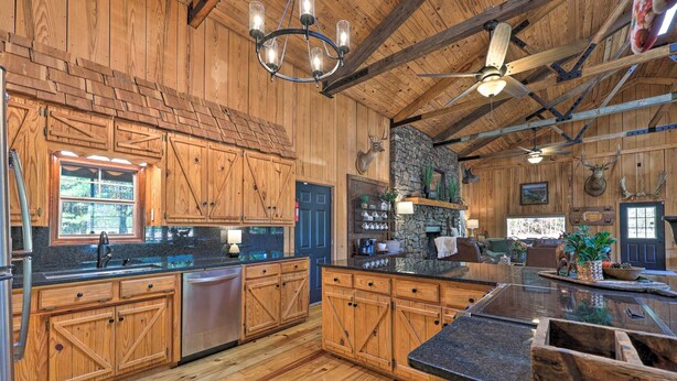 A rustic kitchen with wooden cabinets, a stone fireplace, and a large island with a sink. - Waterfront Deck: Home on Ouachita River! (Arkadelphia)