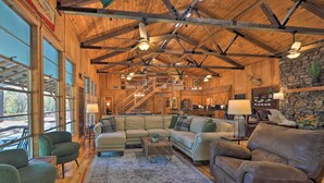 A spacious living room with a large sectional sofa, a leather armchair, and a coffee table. There is a stone fireplace and a staircase leading to an upper level. - Waterfront Deck: Home on Ouachita River! (Arkadelphia)