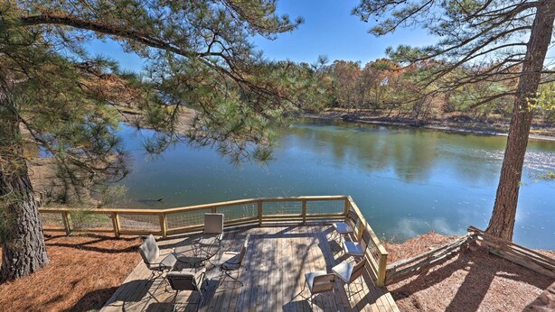 A wooden deck with outdoor seating and a view of a calm lake surrounded by trees. - Waterfront Deck: Home on Ouachita River! (Arkadelphia)