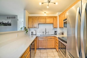 A modern kitchen with wooden cabinets, a stainless steel refrigerator, a built-in oven, and a large window.