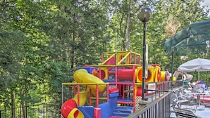A playground with slides and climbing structures surrounded by trees. - Mtn-view Cabin w/ Private Hot Tub in Gatlinburg! (Gatlinburg)