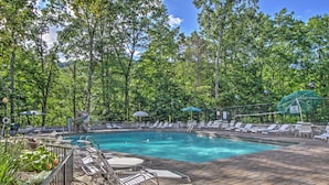 A swimming pool surrounded by trees, with lounge chairs and umbrellas. - Mtn-view Cabin w/ Private Hot Tub in Gatlinburg! (Gatlinburg)