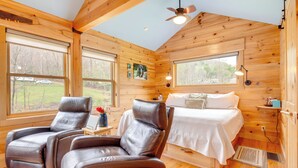 A wooden cabin interior with a bed, two leather recliners, and large windows. - Sawyers Cabin w/ Hot Tub in Blue Ridge Mtns! (Fletcher)