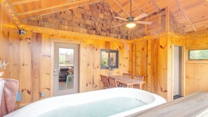 A wooden cabin interior with a hot tub, wooden walls, a dining table, and a ceiling fan. - Sawyers Cabin w/ Hot Tub in Blue Ridge Mtns! (Fletcher)