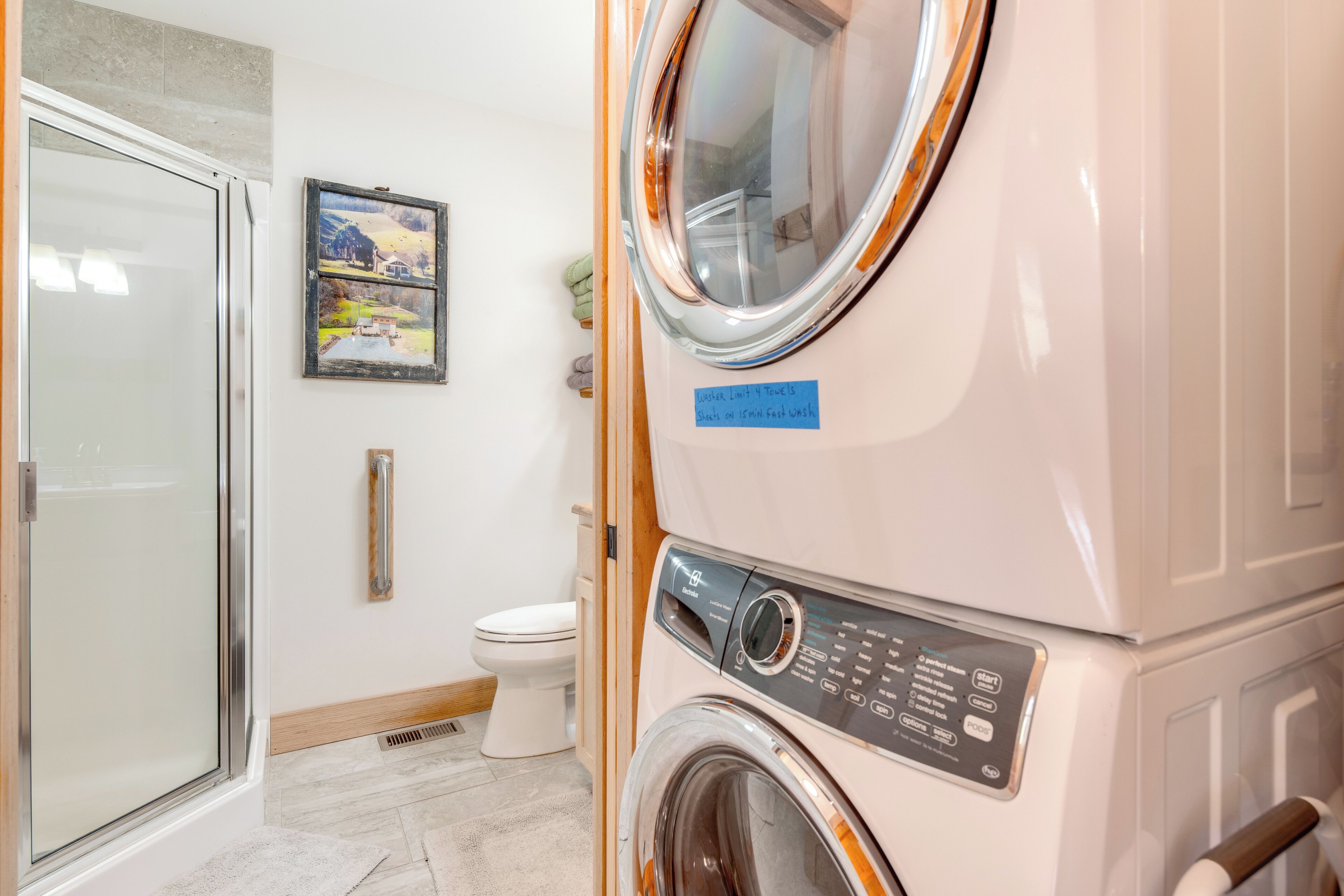 Une buanderie équipée d’une machine à laver et d’un sèche-linge superposés, de toilettes et d’une cabine de douche en verre.