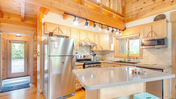A modern kitchen with wooden cabinets, stainless steel appliances, and a central island with stools. - Sawyers Cabin w/ Hot Tub in Blue Ridge Mtns! (Fletcher)