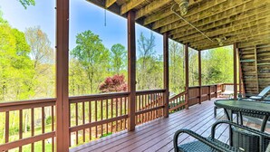 A wooden deck with a table and chairs, surrounded by a wooden railing, overlooking a forested area.