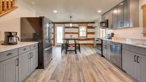 A modern kitchen with grey cabinets, a stainless steel refrigerator, and a wooden dining table.