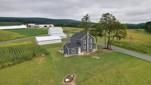 A two-story house with a sloped roof, surrounded by a well-maintained lawn and a cornfield.