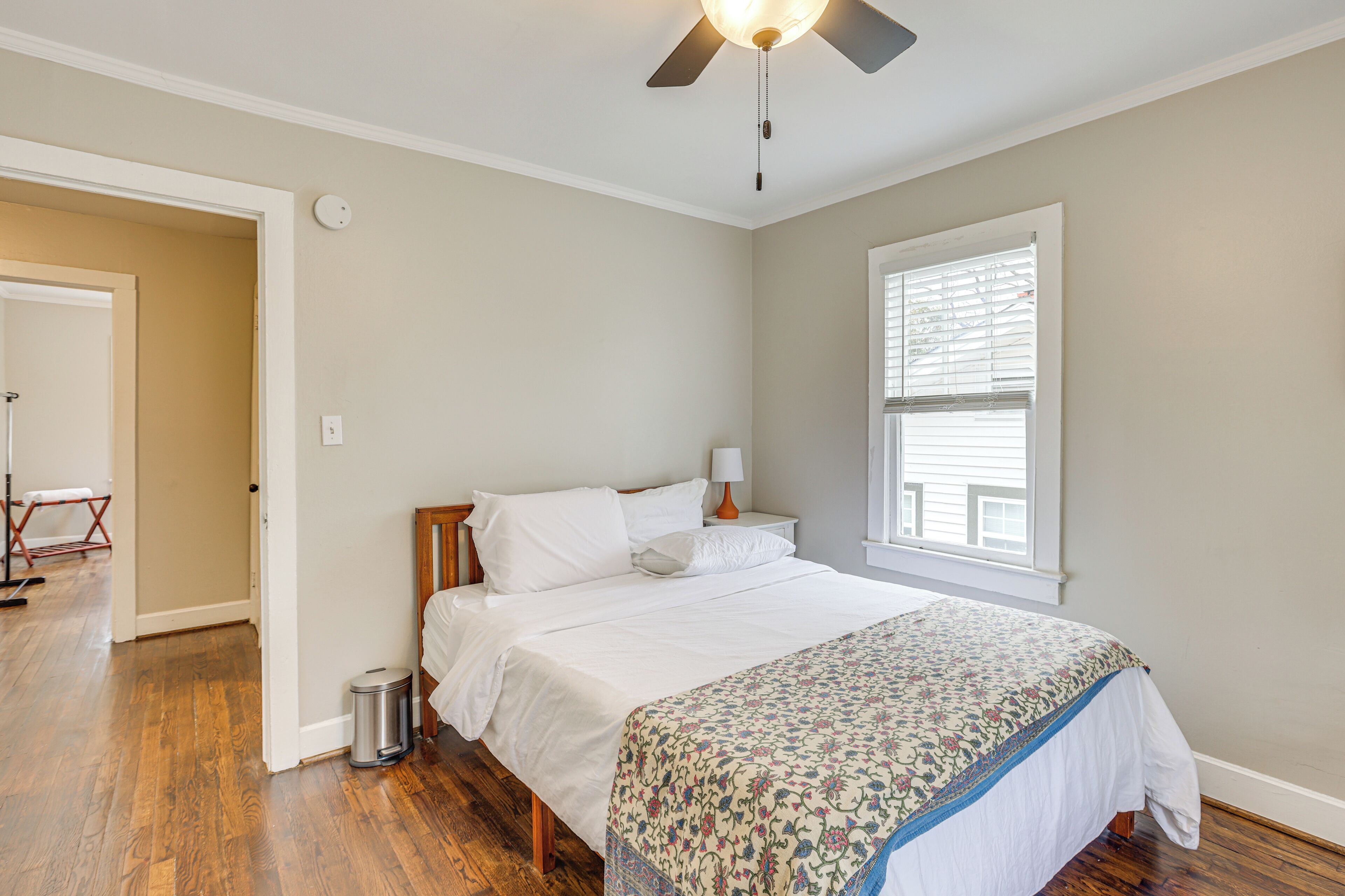 A bedroom with a bed, a ceiling fan, a window with blinds, and a door leading to another room.