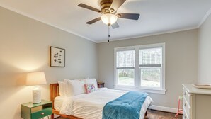 Ein Schlafzimmer mit Bett, Nachttisch, Kommode, Deckenventilator und Fenster.