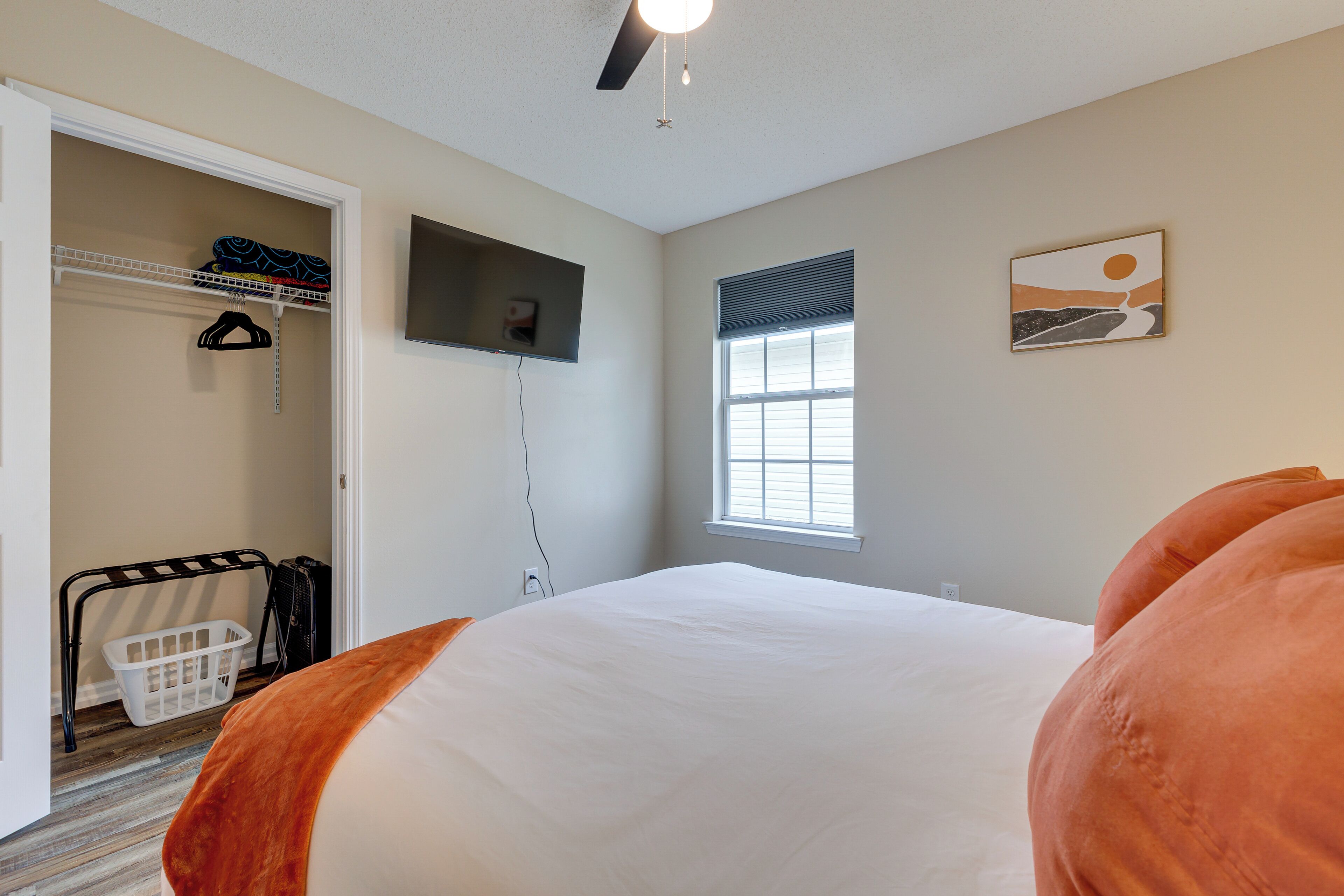 Een slaapkamer met een bed, een kledingkast, een aan de muur bevestigde televisie en een raam met jaloezieën.