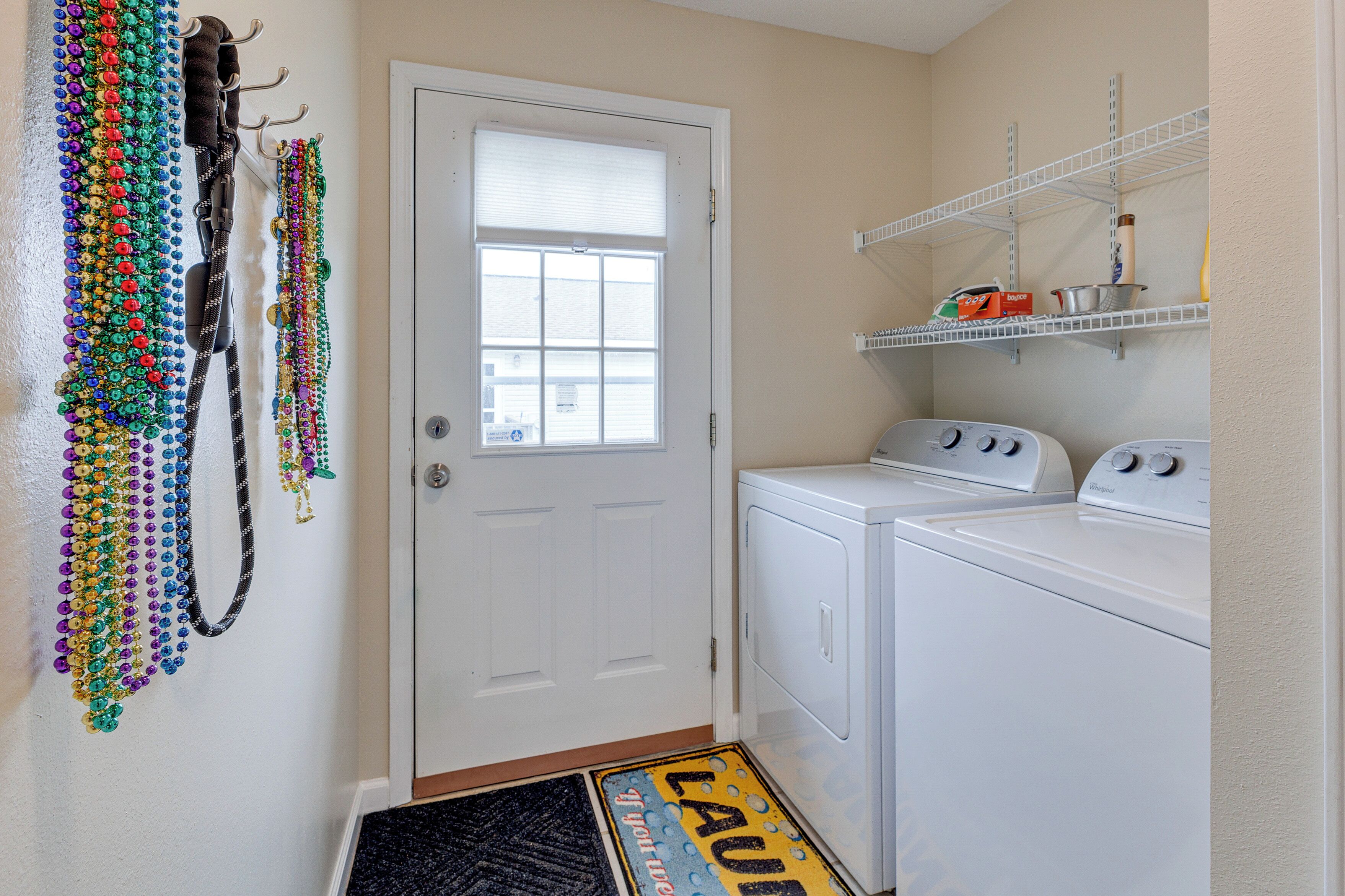 A laundry room with a door, a washing machine, and a shelf with various items.