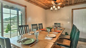 Un comedor con una larga mesa de madera dispuesta para seis personas, rodeada de sillas, y vistas al exterior a través de grandes ventanales.