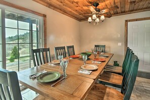 A dining room with a long wooden table set for a meal, surrounded by chairs, and a large window offering a view of the outdoors. - Mountain-view Franklin Retreat: Near Hiking! (Franklin)