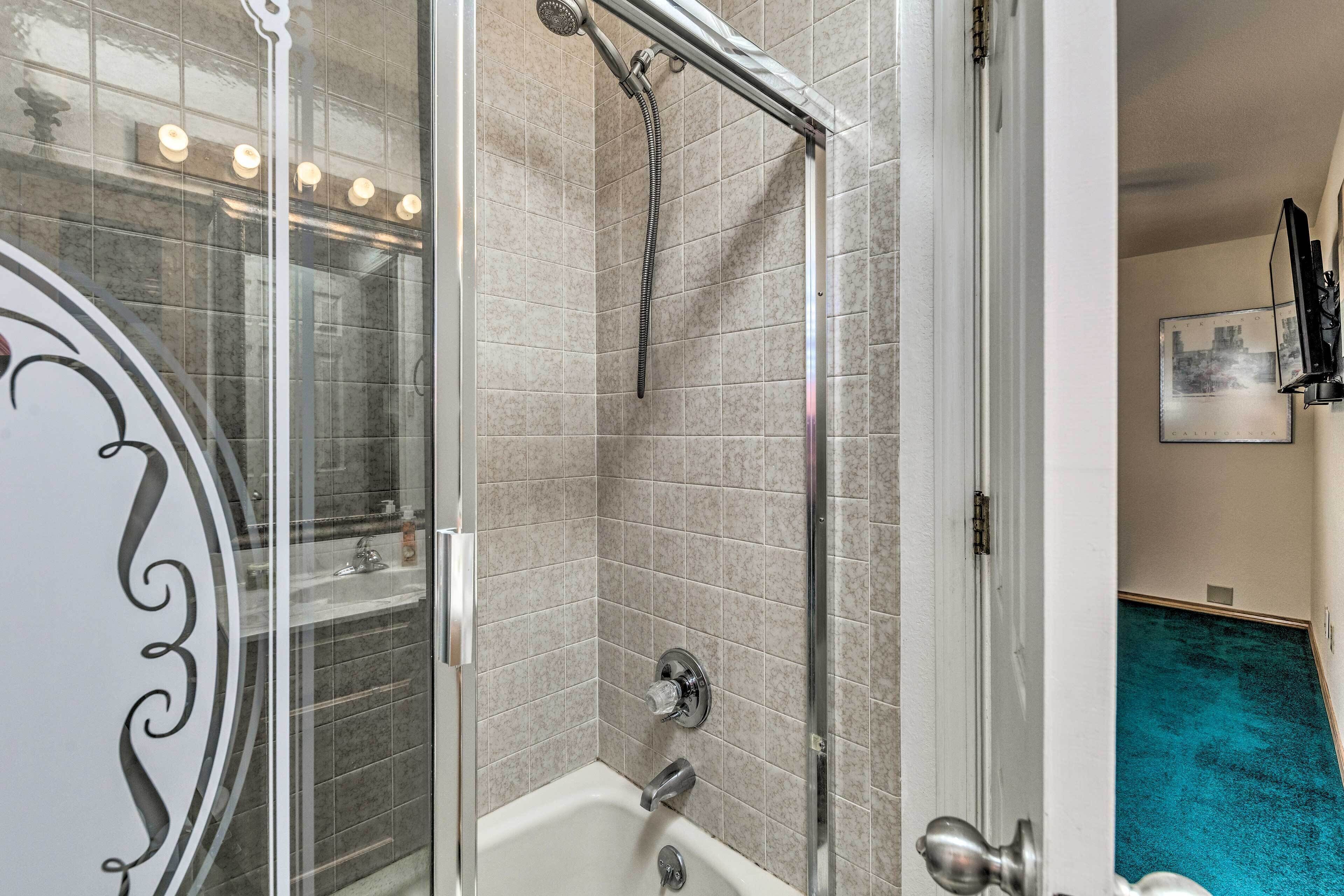 Een badkamer met een douche met glazen wand, een badkuip en een wastafel.