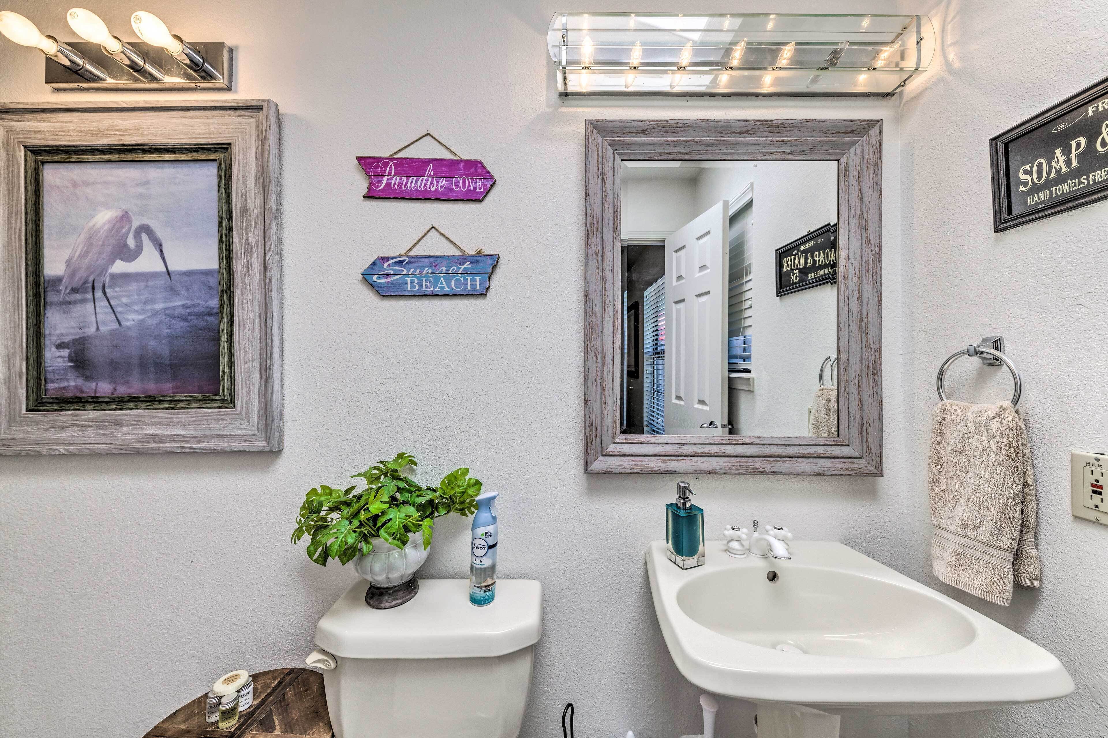 Un baño con inodoro, lavabo y un cuadro enmarcado de un pájaro. Hay carteles en la pared y una planta sobre el inodoro.