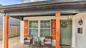 Un patio abrité, doté de meubles en osier et d’une porte verte.
