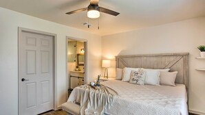 Une chambre à coucher avec un lit, un ventilateur de plafond, une table de chevet avec une lampe et une petite étagère avec une plante.