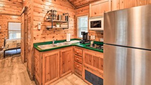 A wooden cabin kitchen with a stainless steel refrigerator, wooden cabinets, a green countertop, and a window with blinds. - Charming New Bern Log Cabin - Pets Welcome! (New Bern)