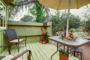 A deck with a table and chairs, surrounded by a green fence, with trees and a pond in the background. - Charming Tiny Home w/ Deck & Pond Access! (Grass Valley)