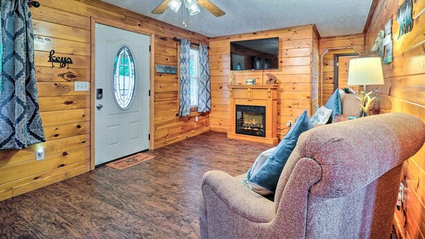 A cozy cabin interior with a wooden interior, a fireplace, a ceiling fan, and a comfortable seating area. - Charming Jamestown Cabin w/ Large Backyard! (Jamestown)