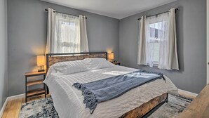 Een slaapkamer met een bed, nachtlampjes, een houten hoofdbord en een raam met gordijnen.