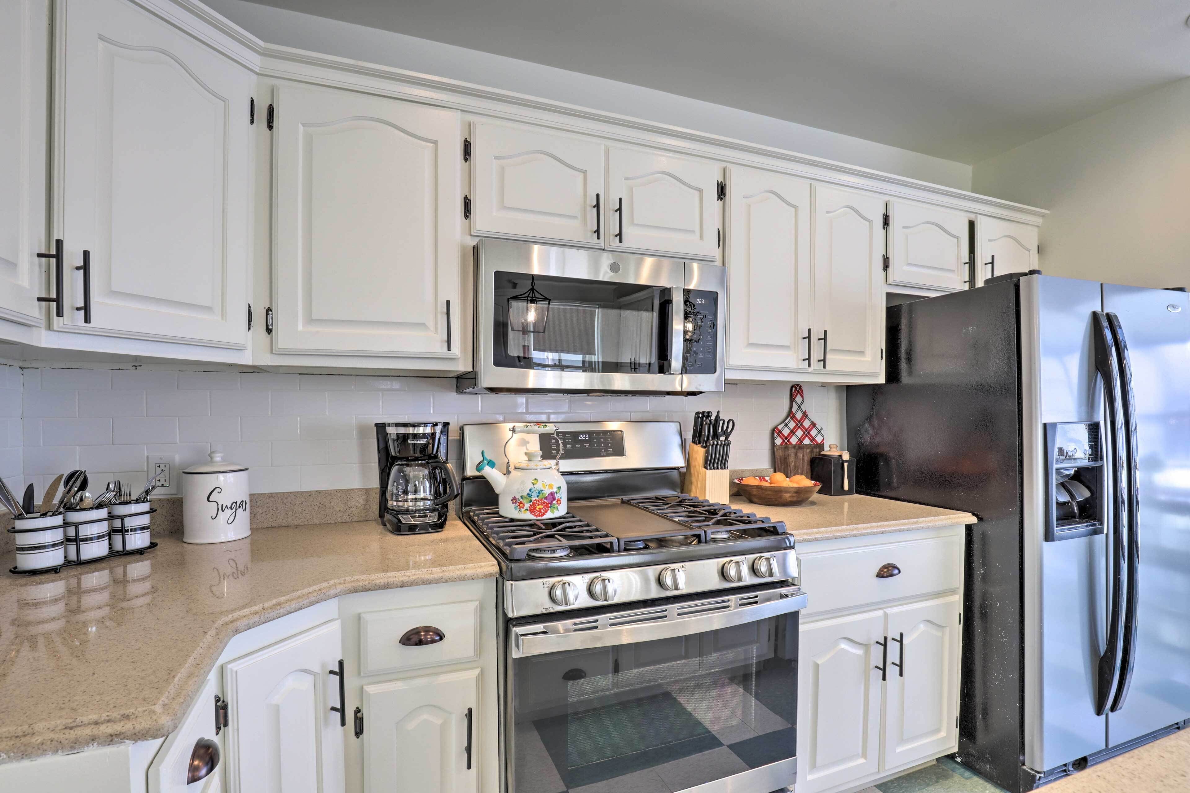 A kitchen with white cabinets, a stainless steel stove, a microwave, and a refrigerator.