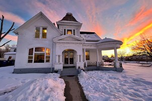 Una casa de estilo victoriano blanca con un porche cubierto y una entrada cubierta de nieve.