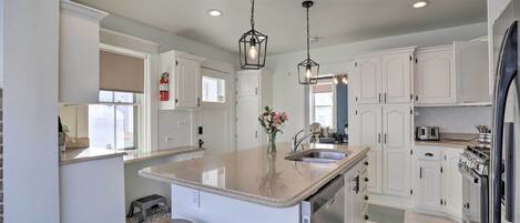 A kitchen with white cabinets, a large island with stools, pendant lighting, and a checkered floor.