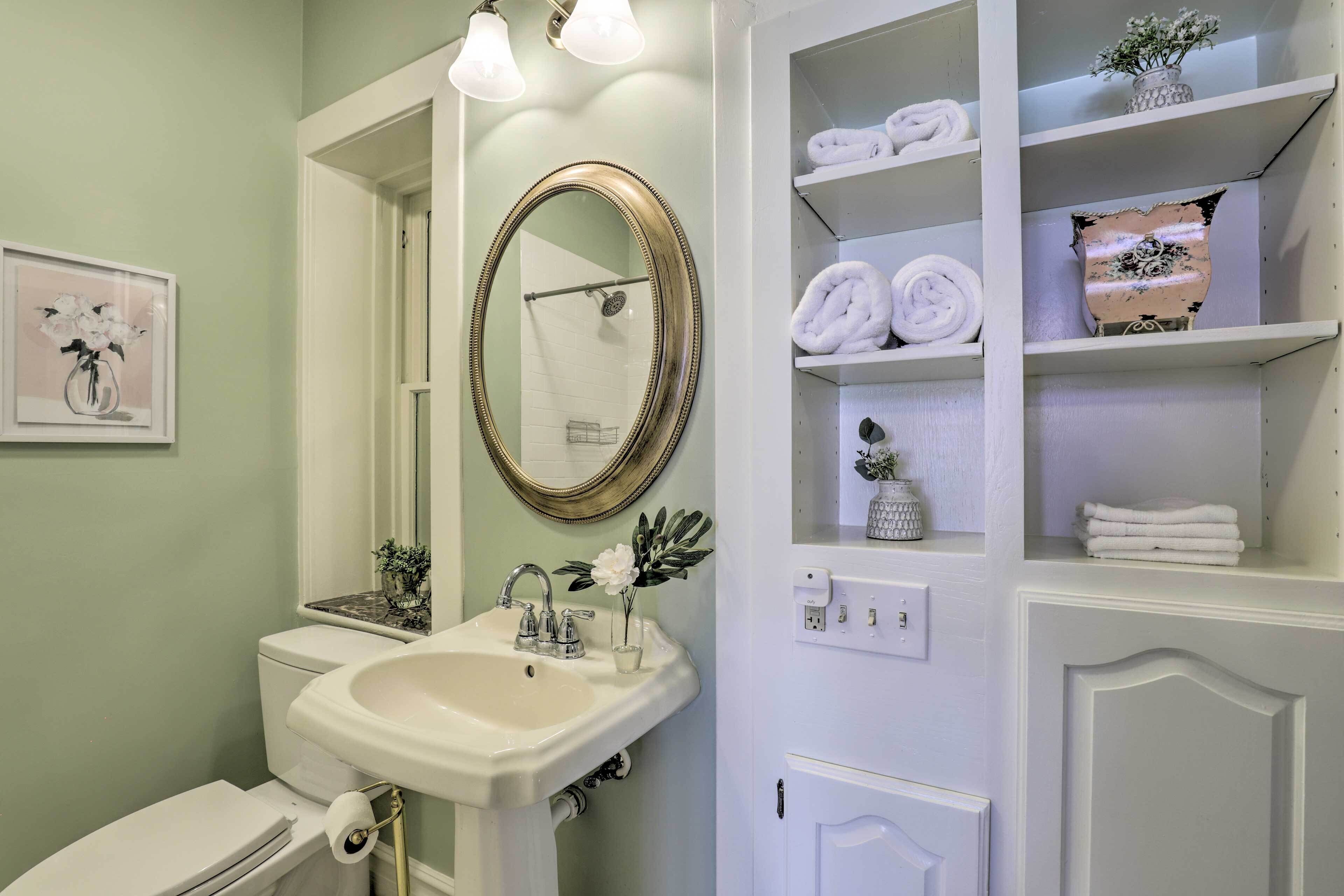A bathroom with a white sink, a mirror, and a shelf with towels.