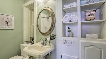A bathroom with a white sink, a mirror, and a shelf with towels.