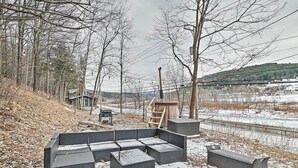 Un espace extérieur aménagé pour l’hiver, avec un canapé et des fauteuils, une terrasse en bois et une vue sur une voie ferrée.