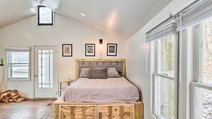 Une chambre à coucher avec un lit posé sur une plateforme en bois, une porte, une fenêtre et des tableaux encadrés accrochés au mur.