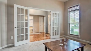 A room with a wooden table, two open doors leading to another room, and a window with blinds. - Great for Groups: Bayside Resort Home w/ Patio (Selbyville)
