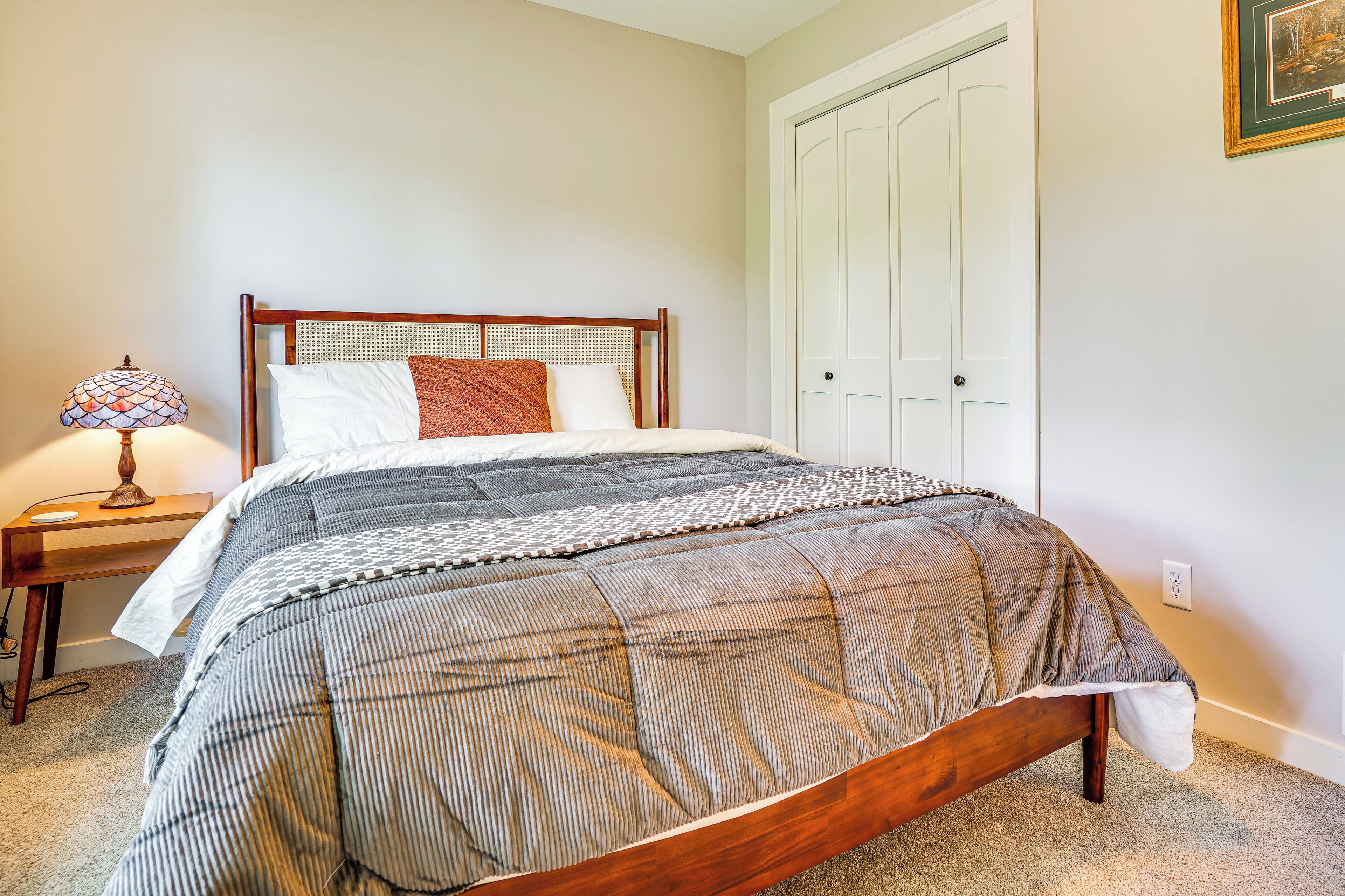 A neatly made bed with a striped bedspread, a wooden headboard, and a bedside lamp on a nightstand.