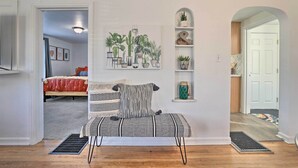 A modern living room with a sofa, a wall-mounted plant illustration, and a hallway leading to another room. - Central Boise Home Near Bsu, 1 Mi to Dtwn! (Boise)