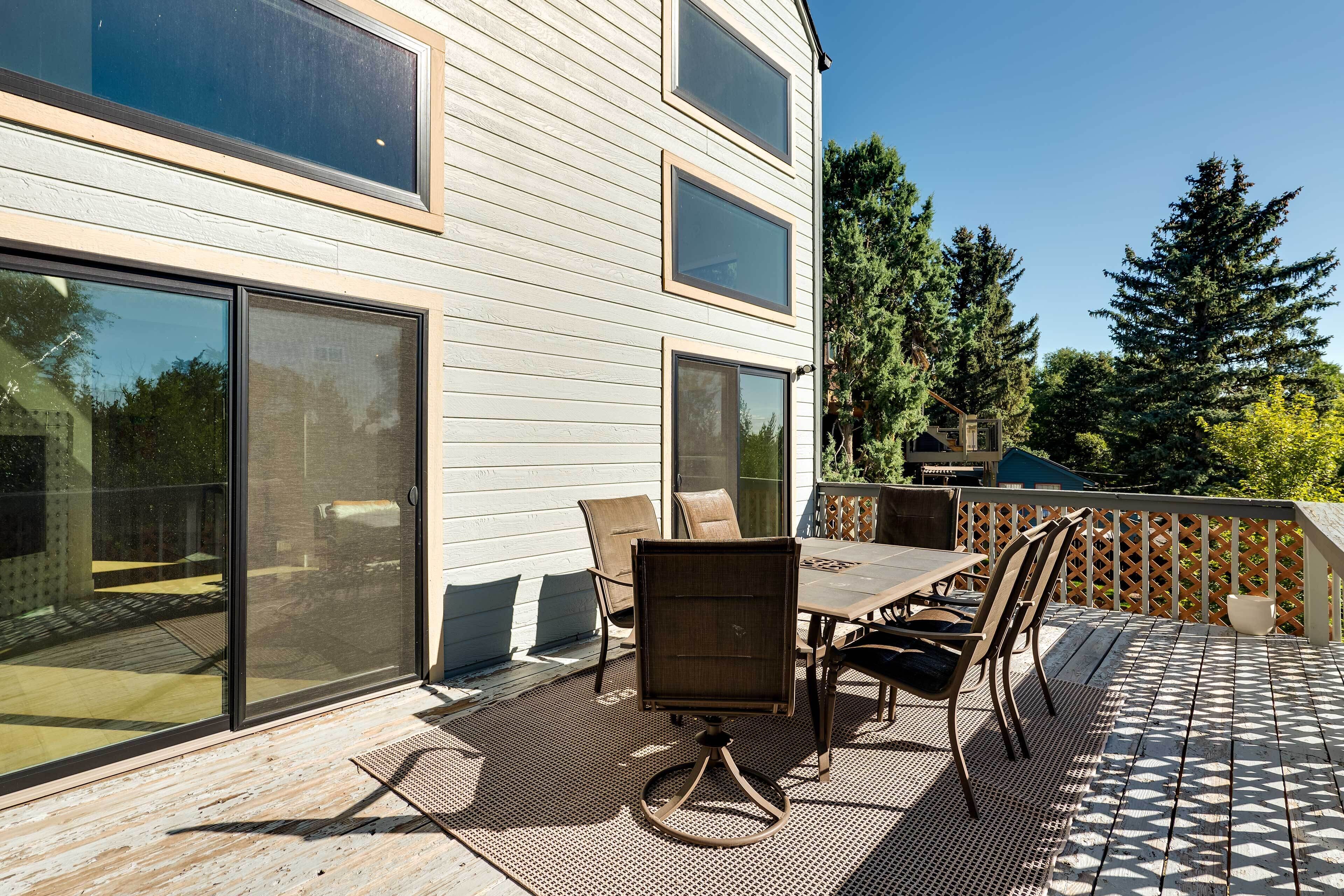 A deck with a table and chairs, a sliding glass door, and a view of a house with large windows and a wooden deck.
