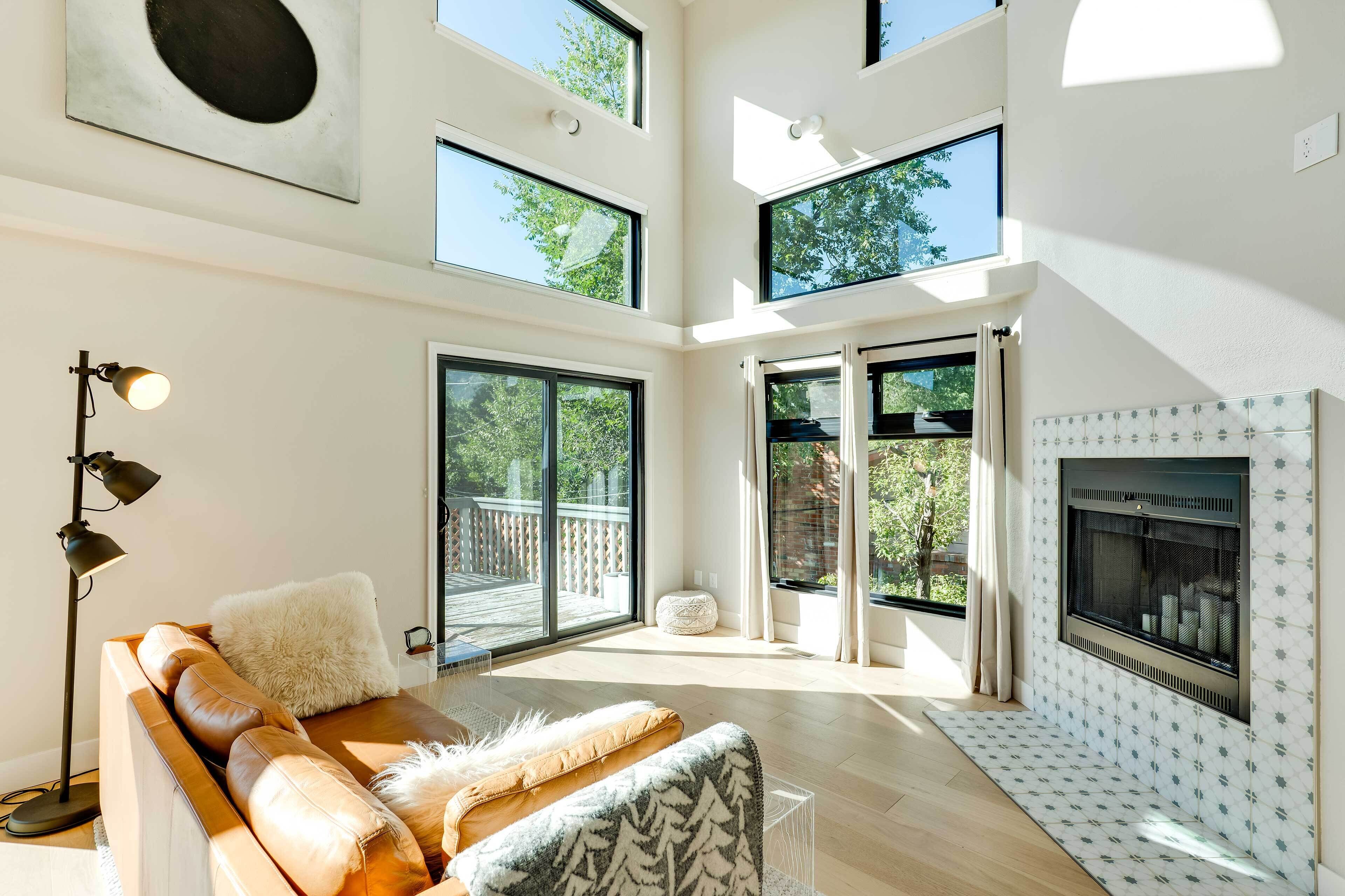 A spacious living room with a high ceiling, large windows, a fireplace, and a modern sofa.