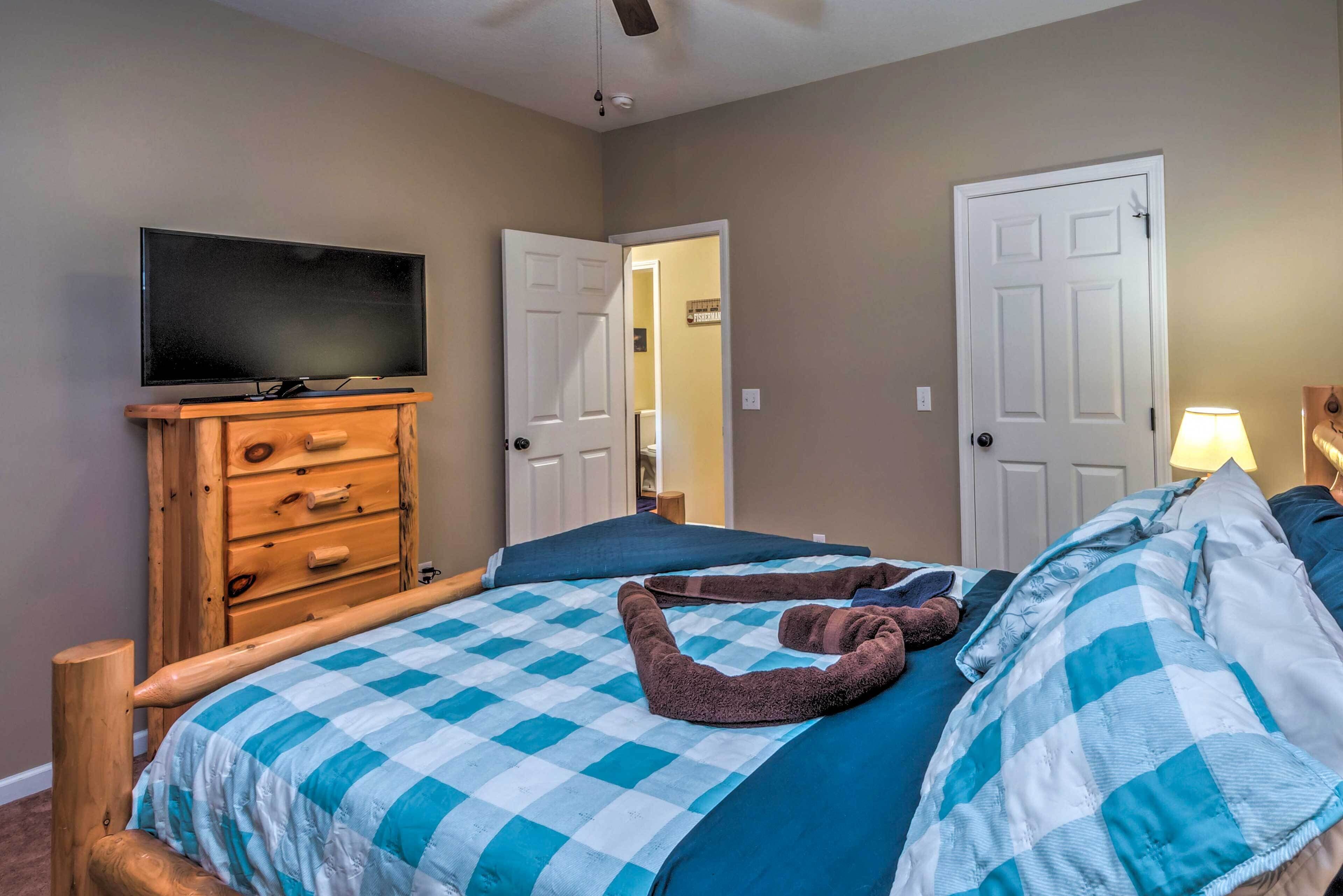 A bedroom with a checkered bedspread, a wooden dresser, a television, and two doors.