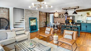 A spacious living area with a wooden floor, leather sofas, a dining table, and a kitchen with blue cabinets. - Chic Troy Home Near Downtown, 9 Mi to Albany! (Troy)