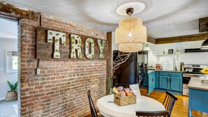 A rustic kitchen with a brick wall, a chandelier, and a table with chairs. - Chic Troy Home Near Downtown, 9 Mi to Albany! (Troy)