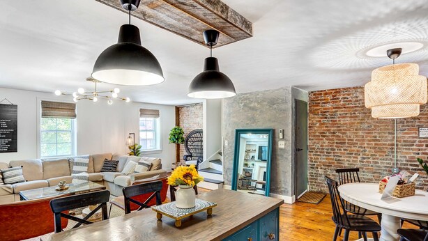 A spacious living area with a wooden dining table, blue cabinets, and a brick wall. - Chic Troy Home Near Downtown, 9 Mi to Albany! (Troy)