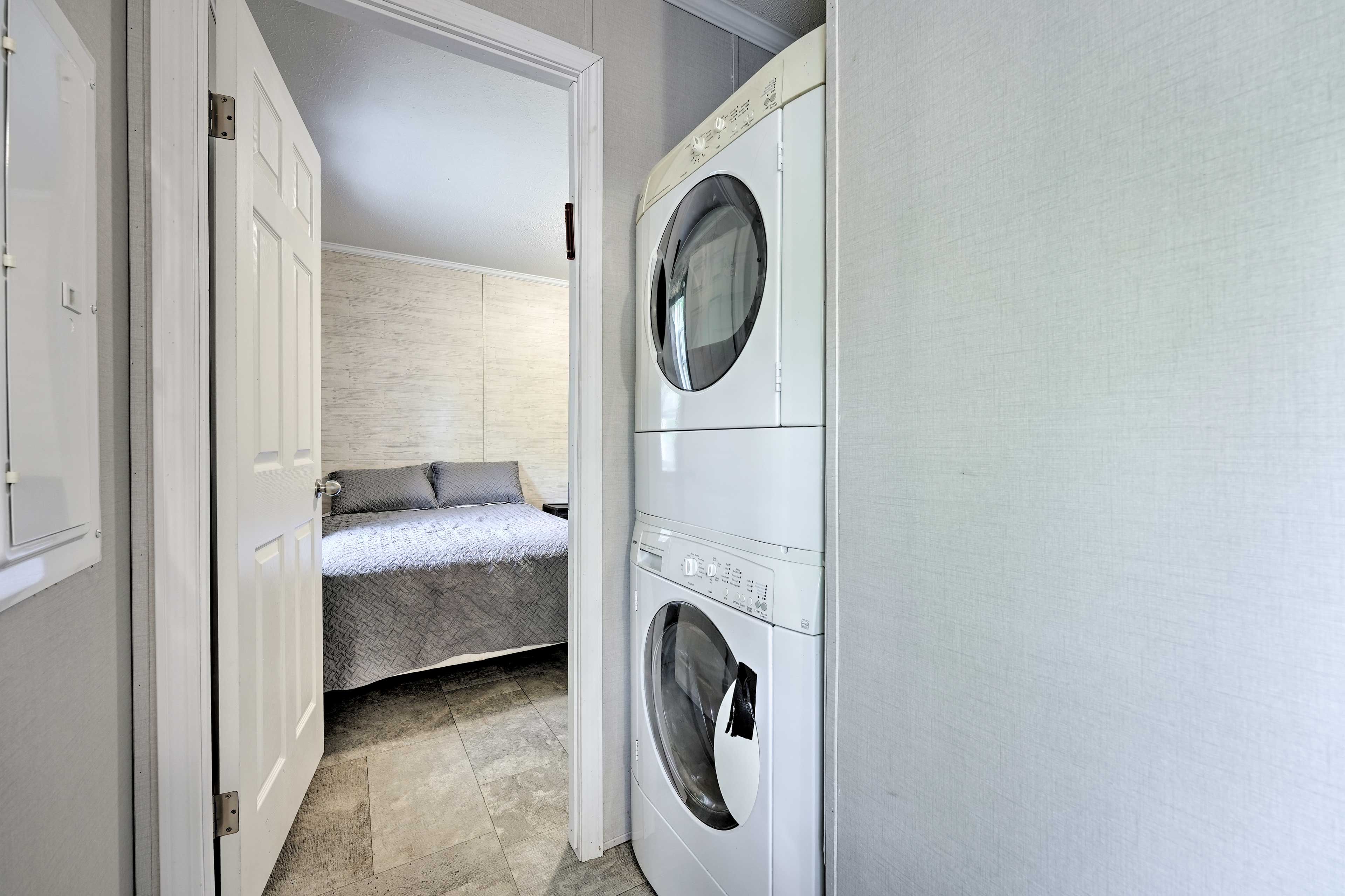 A laundry room with a washing machine and dryer, a bed with a gray quilt, and a door leading to another room.