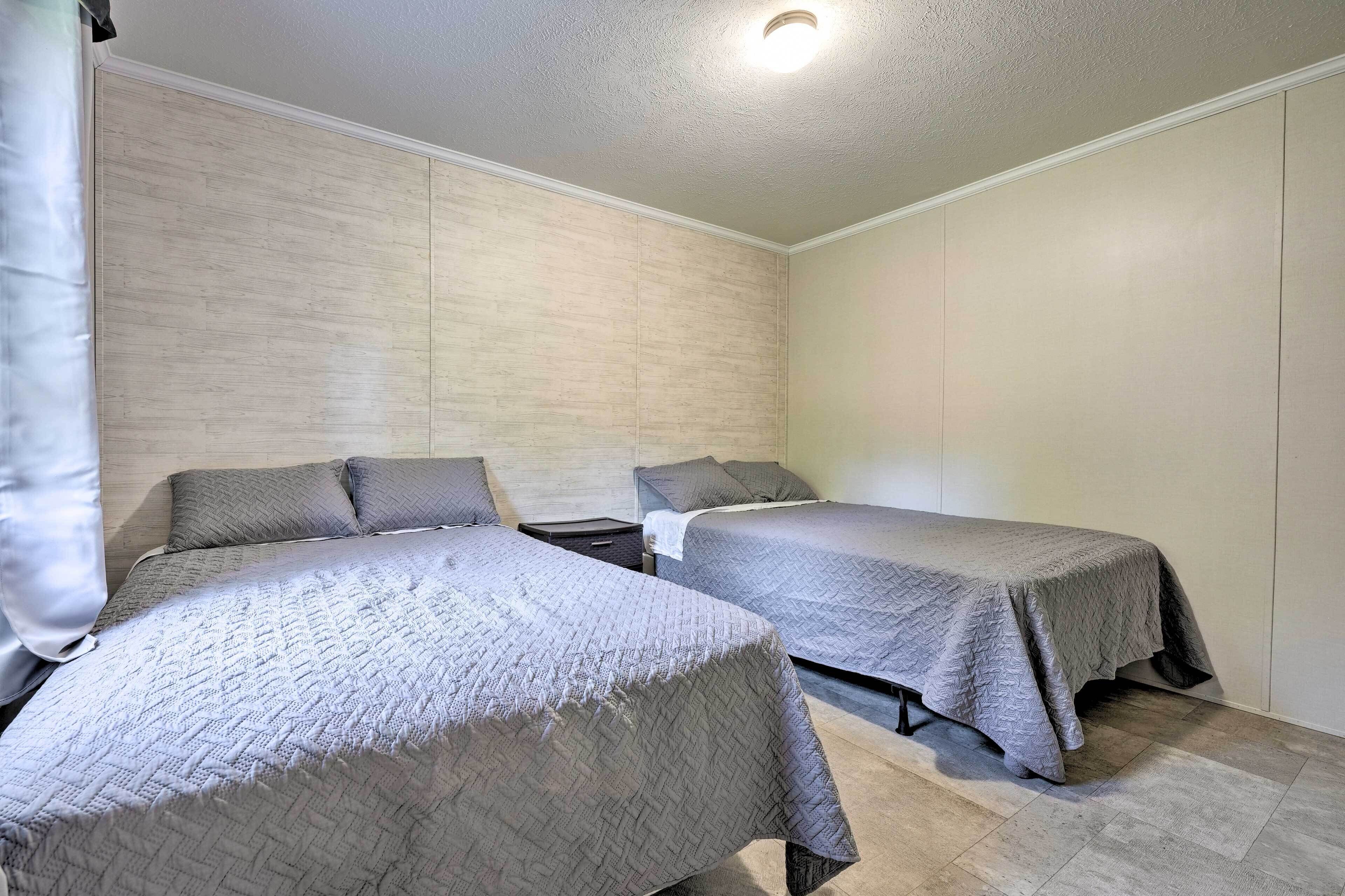Una habitación con dos camas, cada una con colcha gris acolchada y almohadas, una mesita de noche pequeña y un cabecero de madera clara.